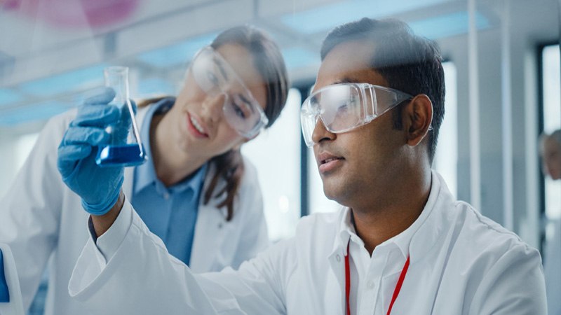 A young female and a male scientist looking at a beaker with blue liquid