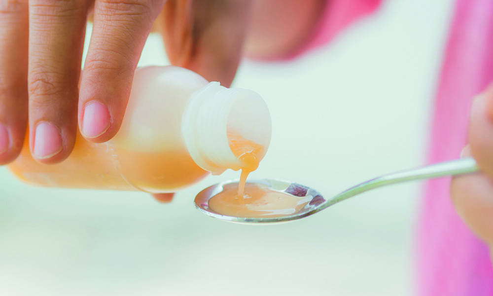 Close-up of children’s syrup formulated with BC Simethicone being poured into a teaspoon for the relief of gas and colic in infants and young children.