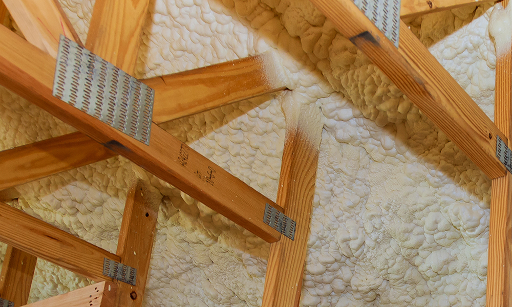 Spray foam insulation applied between wooden roof trusses illustrating special additives for superior energy efficiency in constructions.