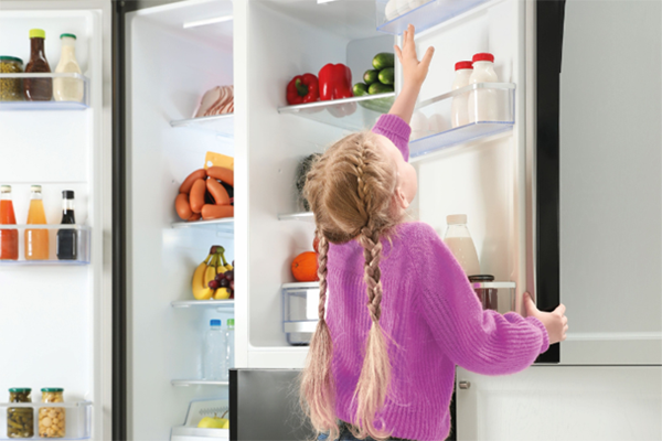 Niña pequeña alcanzando huevos en un refrigerador doméstico de última generación