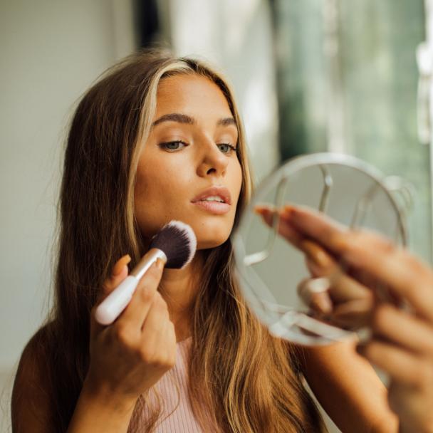 Mulher jovem aplicando maquiagem no espelho