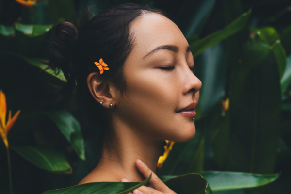 一位美丽的年轻女子，肌肤吹弹可破，妆容淡雅自然，于蕨类植物充满热带风情的翠绿叶片背景前优雅地摆着姿势。一名少女模特用湿发轻触脸部和身体。SPA，养生